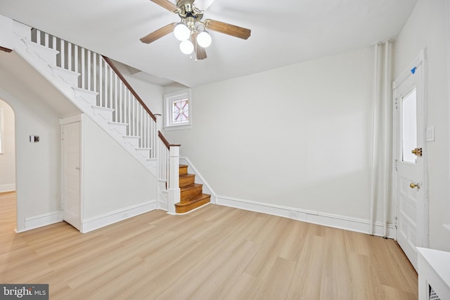 foyer entrance featuring baseboards, arched walkways, a ceiling fan, stairway, and wood finished floors