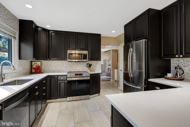 kitchen featuring dark cabinetry, appliances with stainless steel finishes, light countertops, and a sink