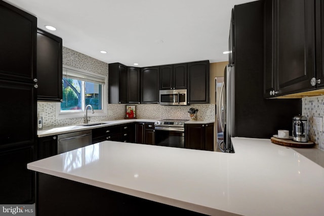 kitchen featuring decorative backsplash, dark cabinets, stainless steel appliances, light countertops, and a sink