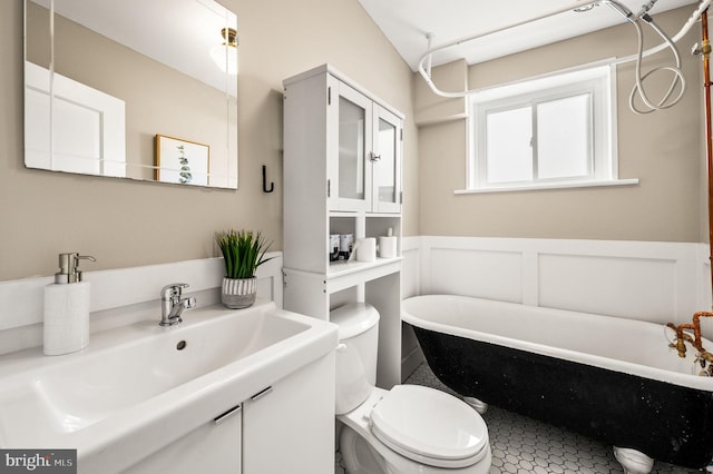 full bath featuring toilet, a decorative wall, a wainscoted wall, vanity, and a soaking tub