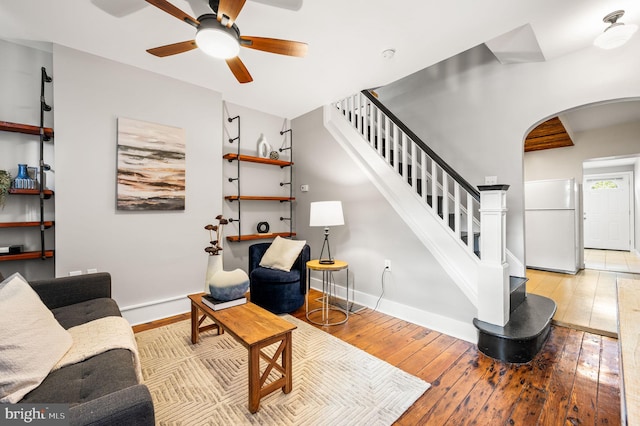 living room with arched walkways, light wood-style flooring, a ceiling fan, baseboards, and stairs