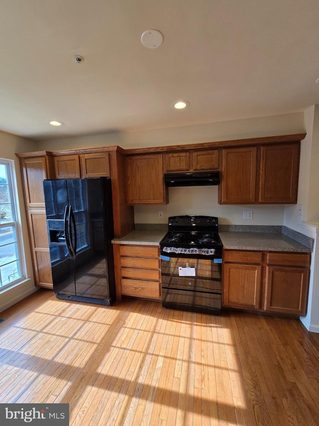 kitchen with light wood-style floors, brown cabinets, under cabinet range hood, black appliances, and recessed lighting