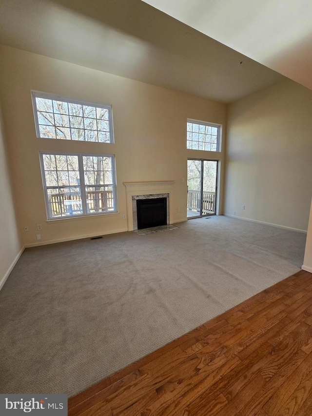 unfurnished living room featuring a towering ceiling, a high end fireplace, visible vents, baseboards, and carpet