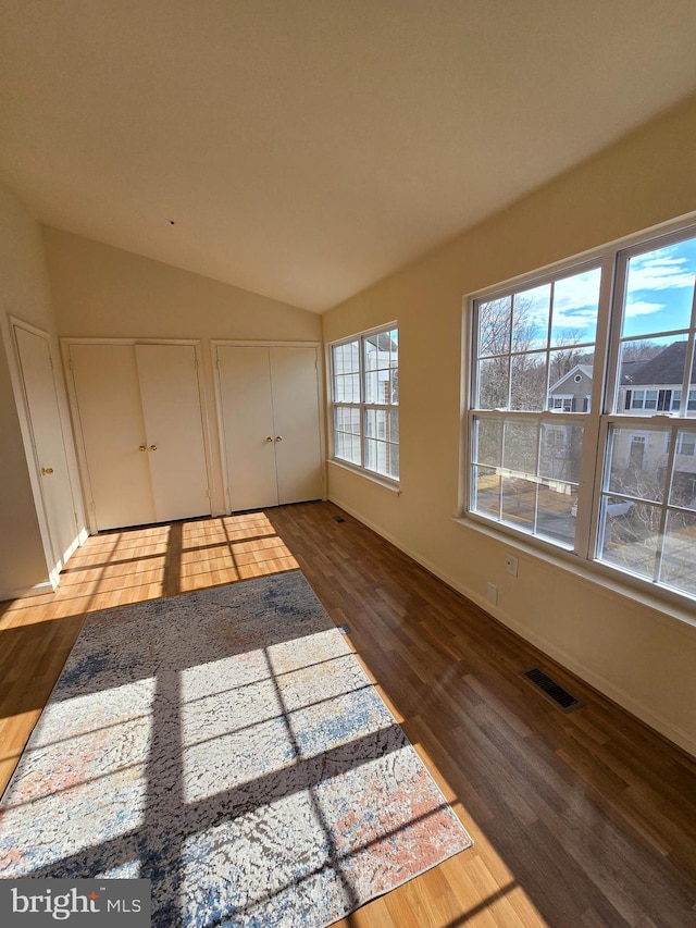 unfurnished bedroom with lofted ceiling, visible vents, multiple closets, and wood finished floors