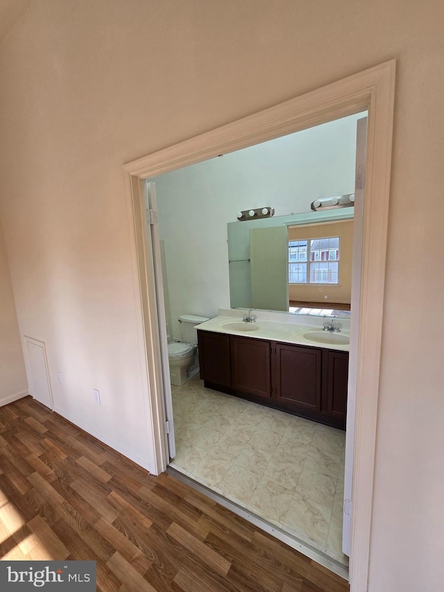 bathroom with double vanity, wood finished floors, a sink, and toilet