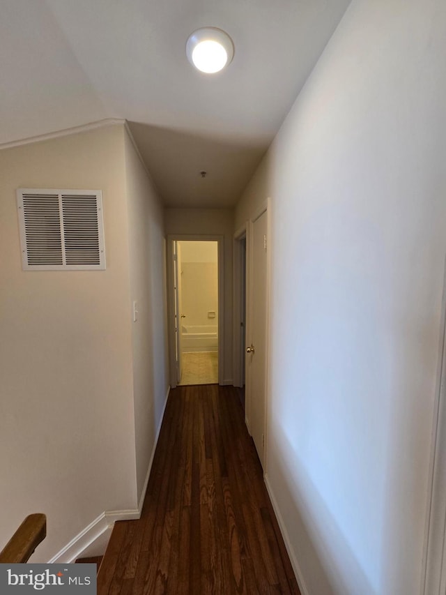 hall featuring dark wood-style flooring, visible vents, and baseboards