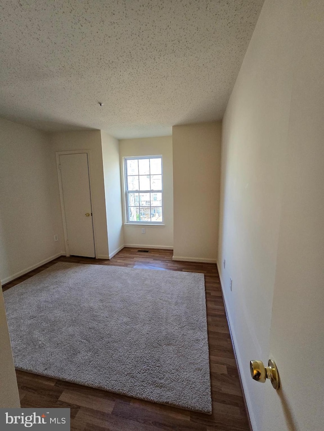 empty room featuring a textured ceiling, baseboards, and wood finished floors