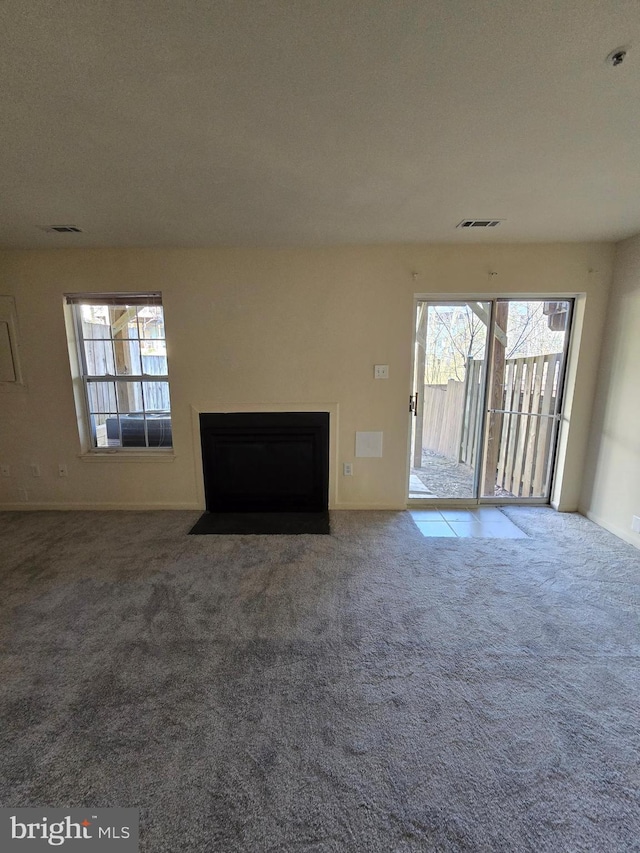 unfurnished living room featuring carpet floors, a fireplace with flush hearth, and visible vents