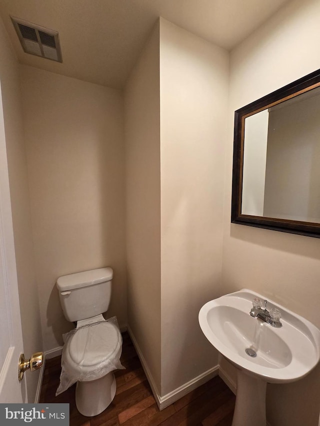 half bathroom featuring baseboards, visible vents, toilet, wood finished floors, and a sink