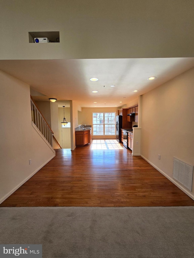 unfurnished living room featuring dark wood-style floors, visible vents, stairway, a sink, and baseboards