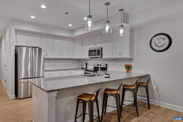 kitchen featuring a peninsula, light stone countertops, white cabinetry, and appliances with stainless steel finishes