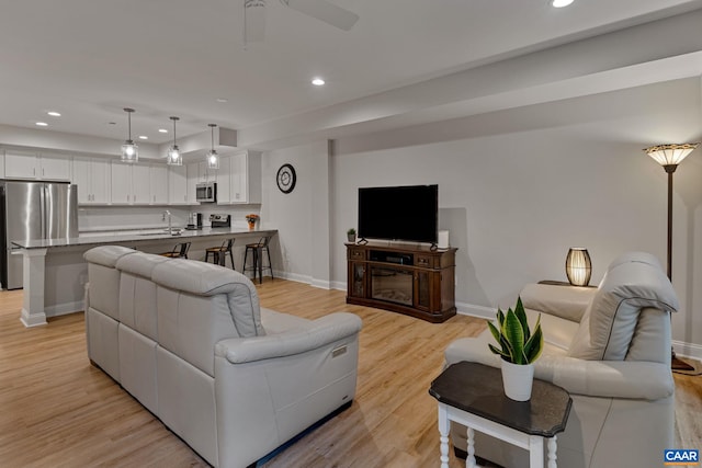 living area with baseboards, light wood-type flooring, a ceiling fan, and recessed lighting