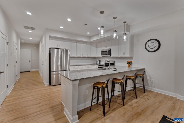 kitchen with a peninsula, appliances with stainless steel finishes, white cabinetry, and pendant lighting