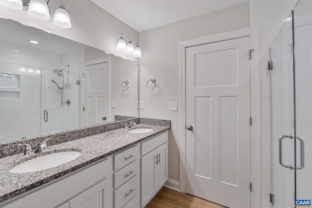 bathroom with double vanity, a shower stall, a sink, and wood finished floors