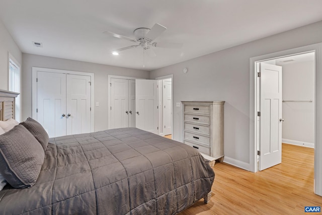 bedroom featuring baseboards, visible vents, ceiling fan, light wood-type flooring, and two closets