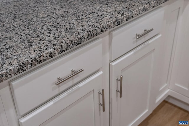 room details with wood finished floors, white cabinets, and light stone countertops