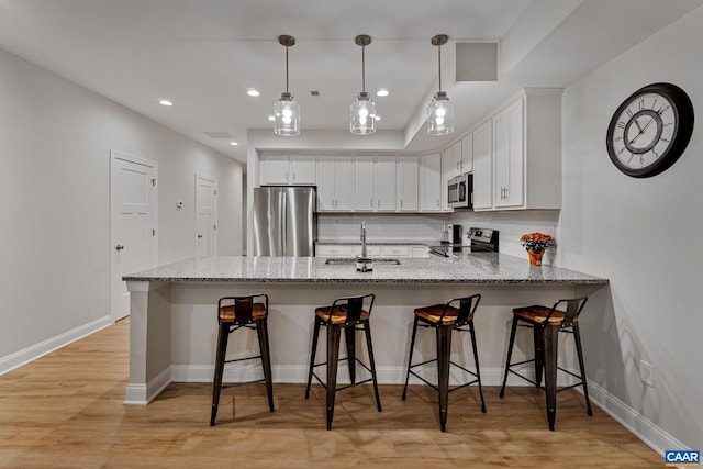 kitchen with appliances with stainless steel finishes, a breakfast bar, decorative light fixtures, a peninsula, and white cabinetry