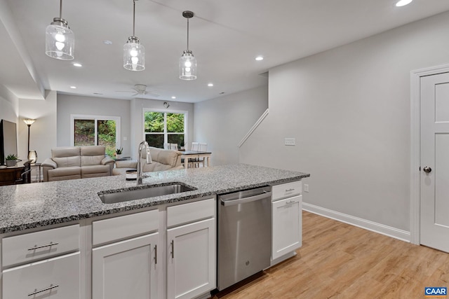 kitchen with white cabinets, dishwasher, open floor plan, light stone countertops, and a sink