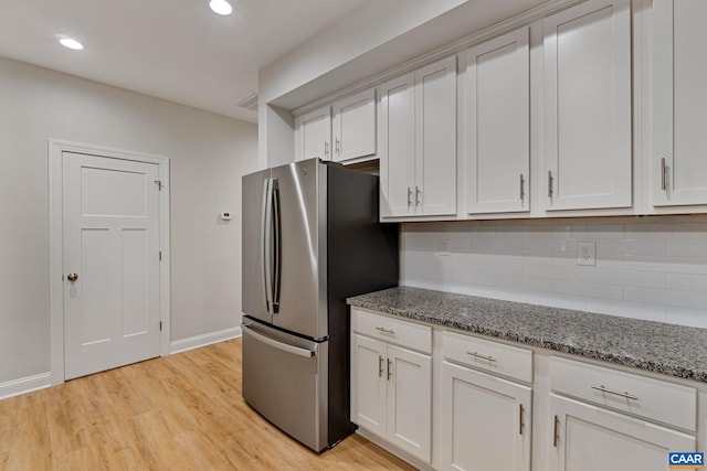 kitchen with light stone counters, freestanding refrigerator, white cabinetry, and backsplash