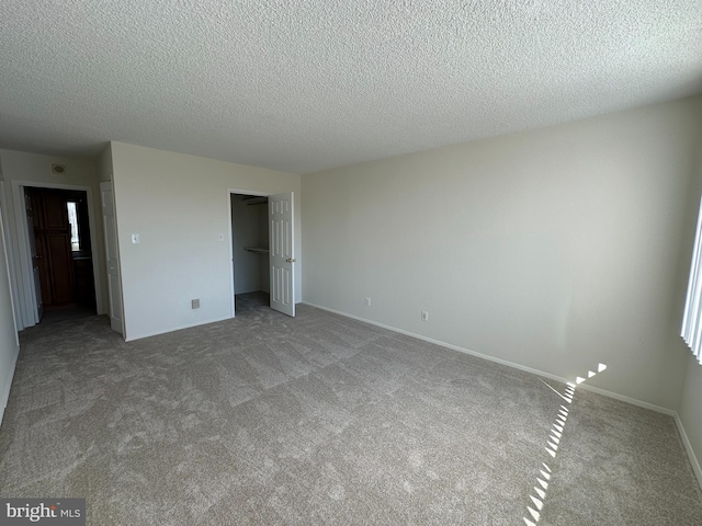 unfurnished bedroom featuring a textured ceiling, a closet, light colored carpet, and baseboards