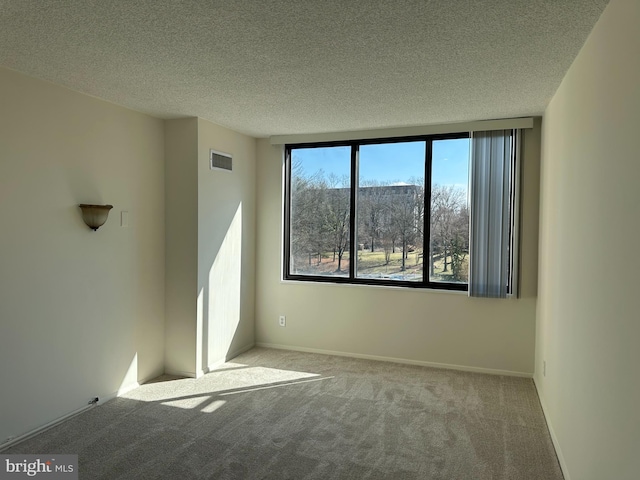 spare room with light carpet, baseboards, visible vents, and a textured ceiling