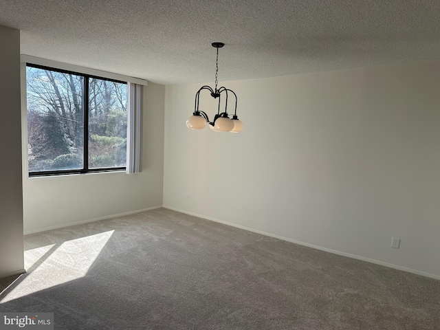 carpeted empty room with a notable chandelier, a textured ceiling, and baseboards