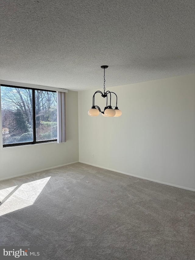 spare room with a chandelier, carpet, a textured ceiling, and baseboards