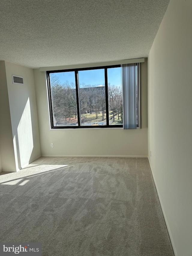 empty room featuring carpet, a healthy amount of sunlight, visible vents, and a textured ceiling