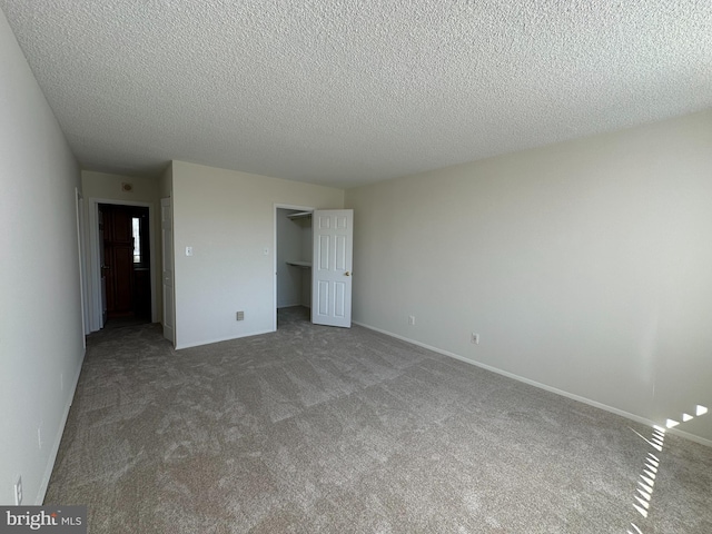 unfurnished bedroom featuring a textured ceiling, carpet flooring, baseboards, a closet, and a walk in closet