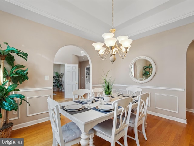 dining space with arched walkways, baseboards, a notable chandelier, and light wood finished floors