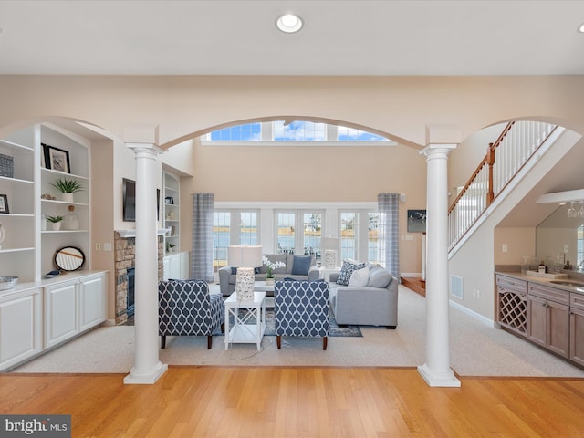 living area with visible vents, a stone fireplace, decorative columns, and light wood-style floors