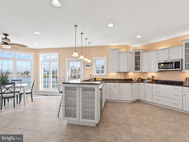 kitchen featuring stainless steel microwave, glass insert cabinets, decorative light fixtures, a peninsula, and recessed lighting