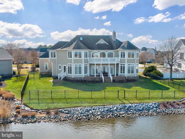 back of house featuring a balcony, a water view, a fenced front yard, and a lawn