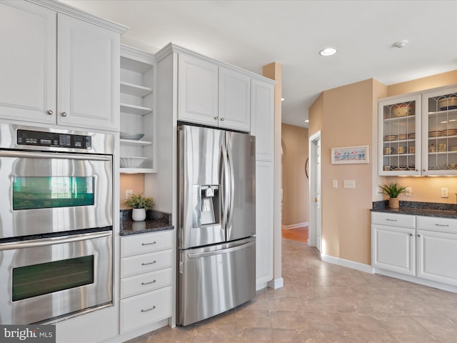 kitchen featuring open shelves, appliances with stainless steel finishes, glass insert cabinets, white cabinets, and dark stone counters