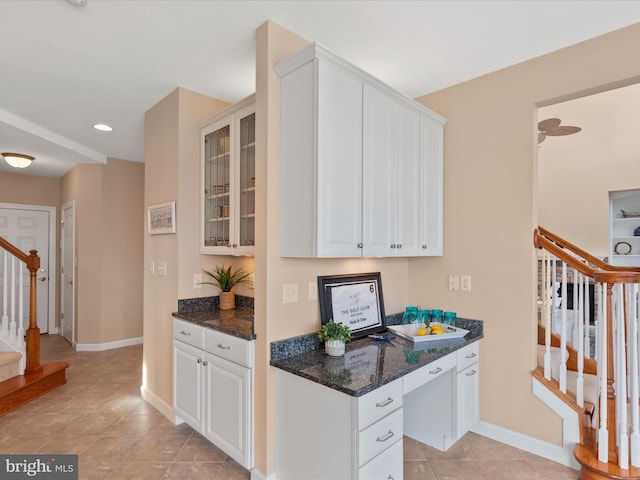 kitchen with light tile patterned floors, white cabinetry, baseboards, dark stone countertops, and glass insert cabinets