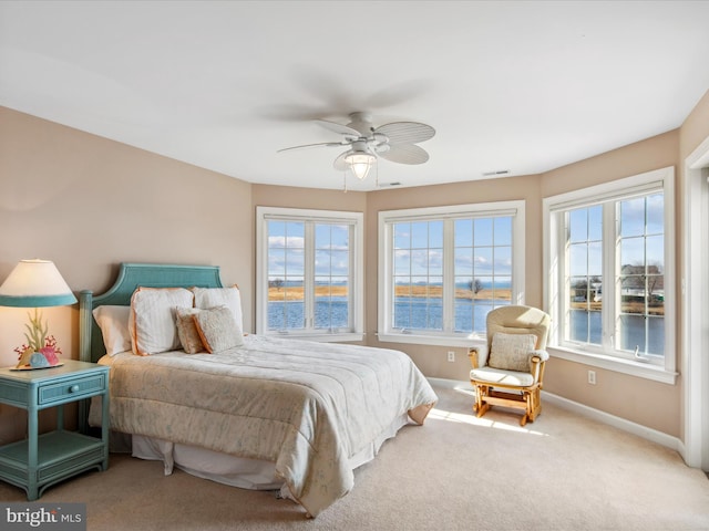 carpeted bedroom featuring a water view, baseboards, multiple windows, and visible vents