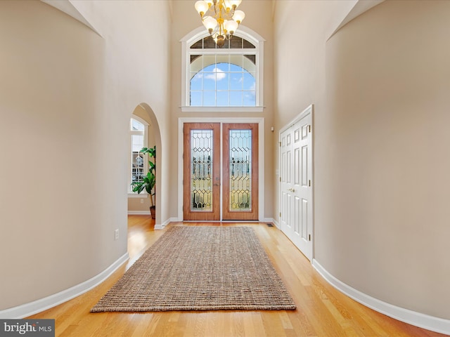 entrance foyer with arched walkways, a notable chandelier, baseboards, and wood finished floors