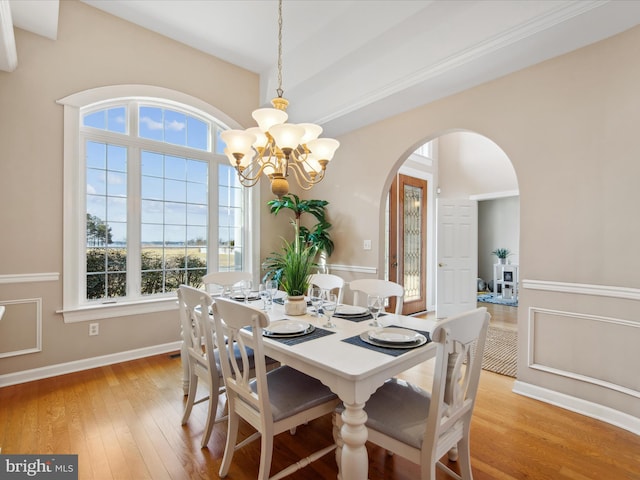 dining room with a chandelier, arched walkways, light wood-style flooring, and baseboards