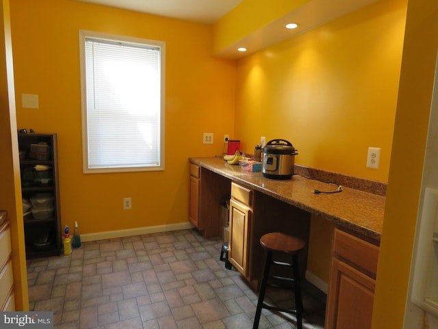 interior space with recessed lighting, baseboards, brown cabinets, built in desk, and stone finish floor