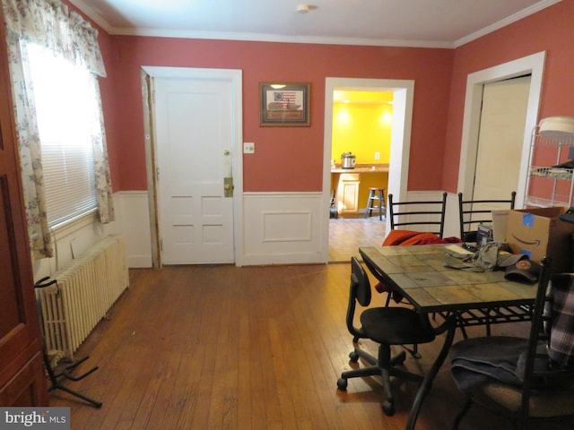 dining space featuring hardwood / wood-style floors, radiator heating unit, wainscoting, and crown molding