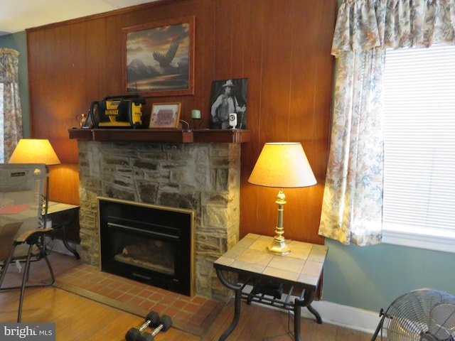 sitting room featuring wooden walls, a stone fireplace, baseboards, and wood finished floors