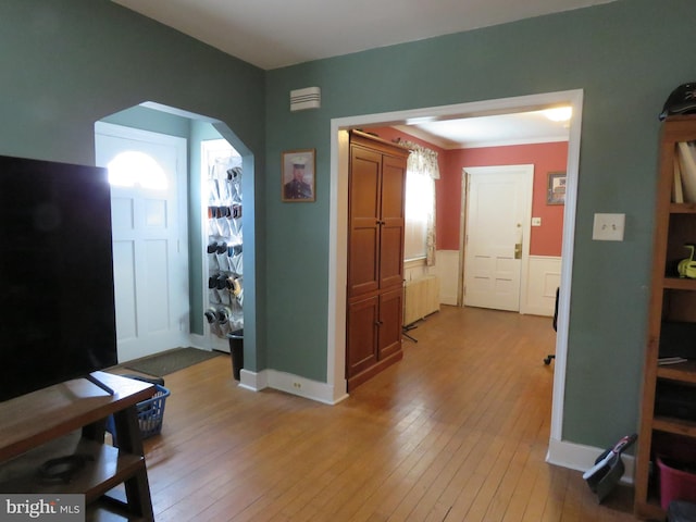 entryway with arched walkways, a wainscoted wall, light wood-style flooring, and radiator