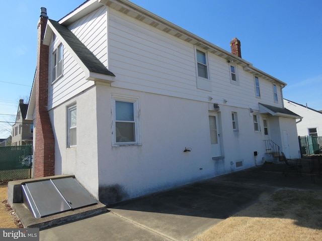 rear view of property featuring roof with shingles, a chimney, and stucco siding