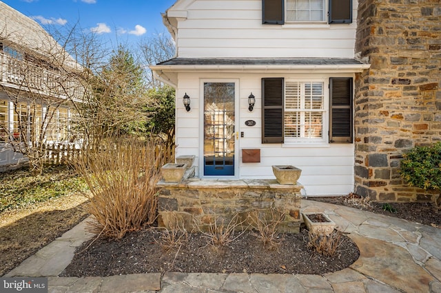 entrance to property with stone siding and a shingled roof