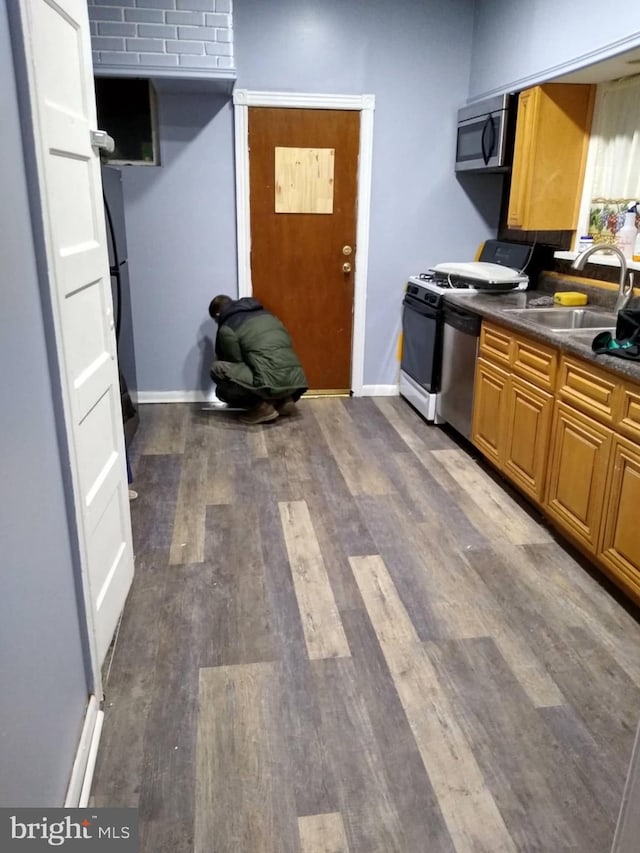 kitchen featuring dark countertops, stainless steel microwave, brown cabinetry, and dark wood-style flooring