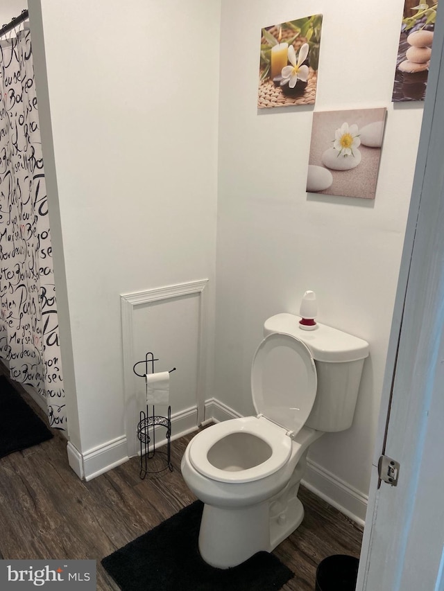 bathroom featuring toilet, curtained shower, baseboards, and wood finished floors