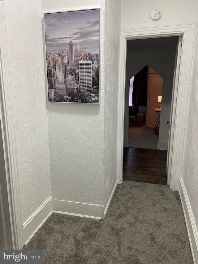 hall with arched walkways, carpet flooring, a textured wall, and baseboards