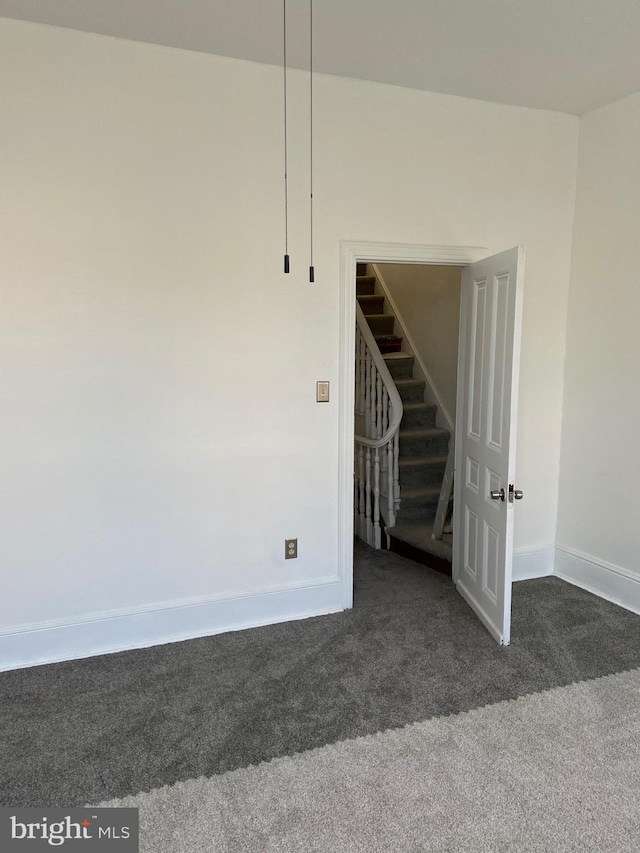 carpeted empty room featuring stairway and baseboards