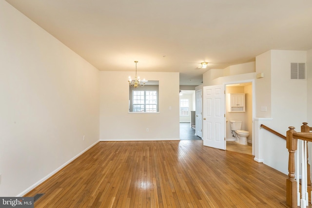 empty room with an inviting chandelier, hardwood / wood-style flooring, baseboards, and visible vents