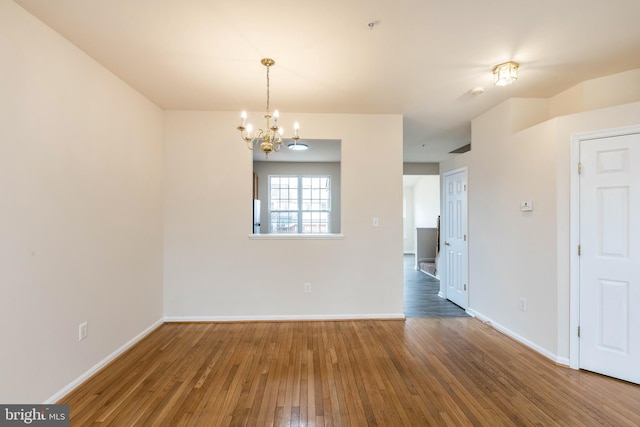 empty room with baseboards, wood-type flooring, and an inviting chandelier